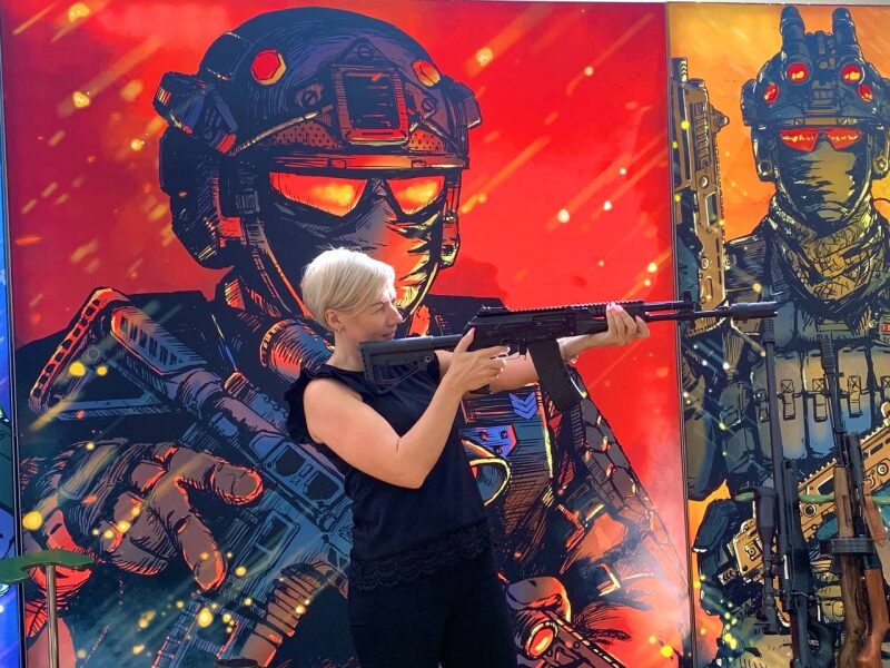 Женщина с автоматом на фоне арт-персонажей LASERWAR.